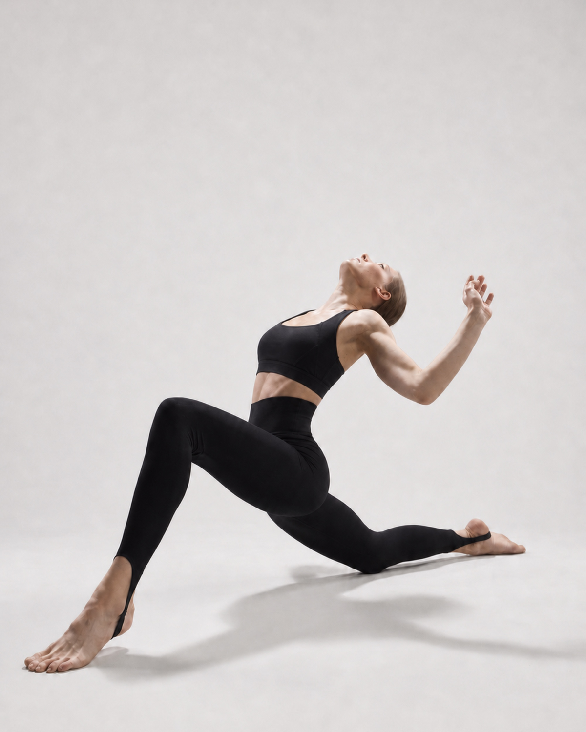 Model wearing black stirrup leggings during a studio stretch, with the underfoot construction visible
